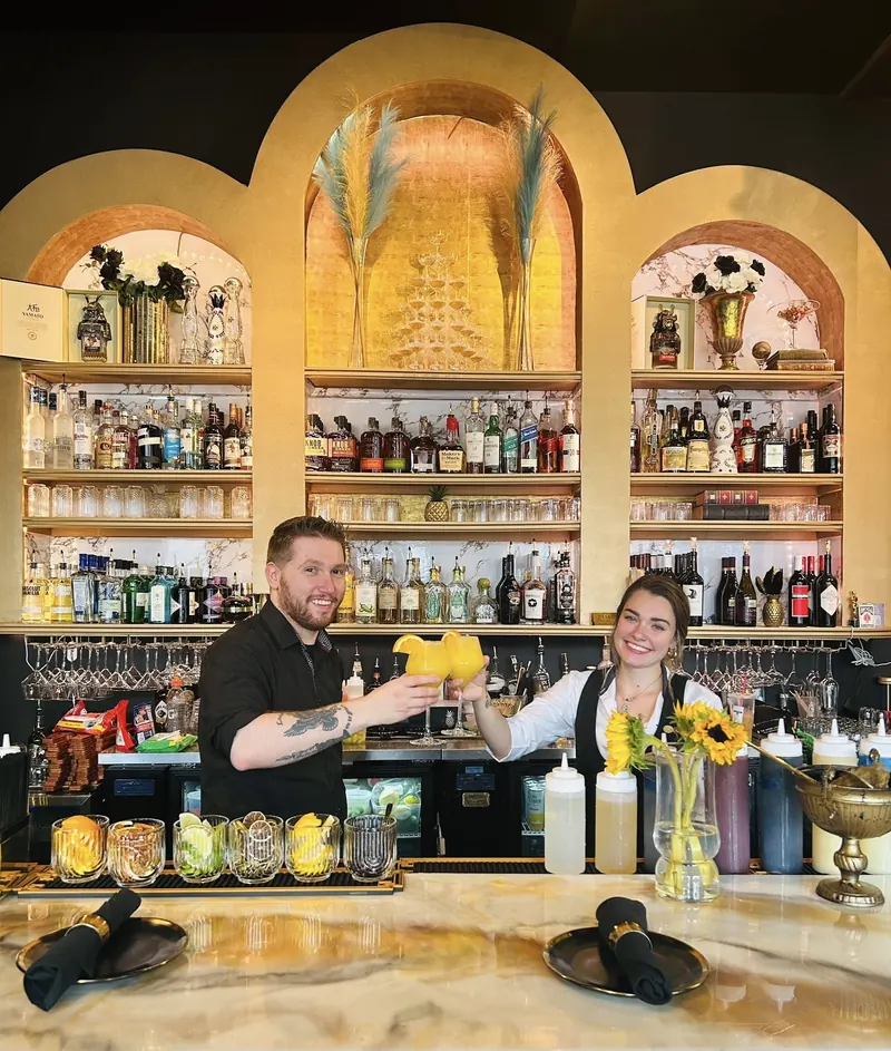 Bartenders at work in front of the gold arched back bar and pineapple mural