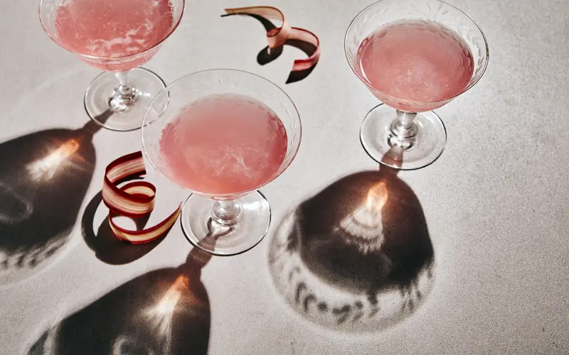 Three coupe glasses of blush-pink cosmos casting long shadows