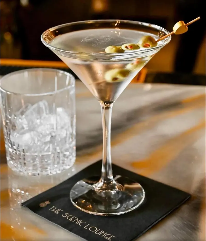 A martini with three olives on a Scenic Lounge napkin, backlit at the bar