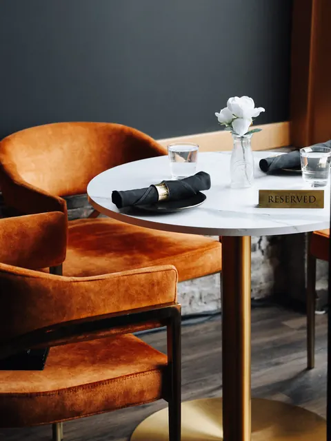 A reserved marble table with a white rose, flanked by rust velvet chairs