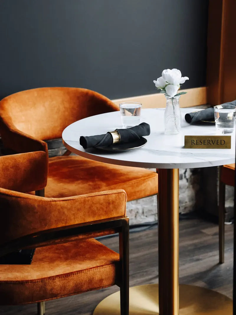 A reserved marble table set with a white rose between rust velvet armchairs